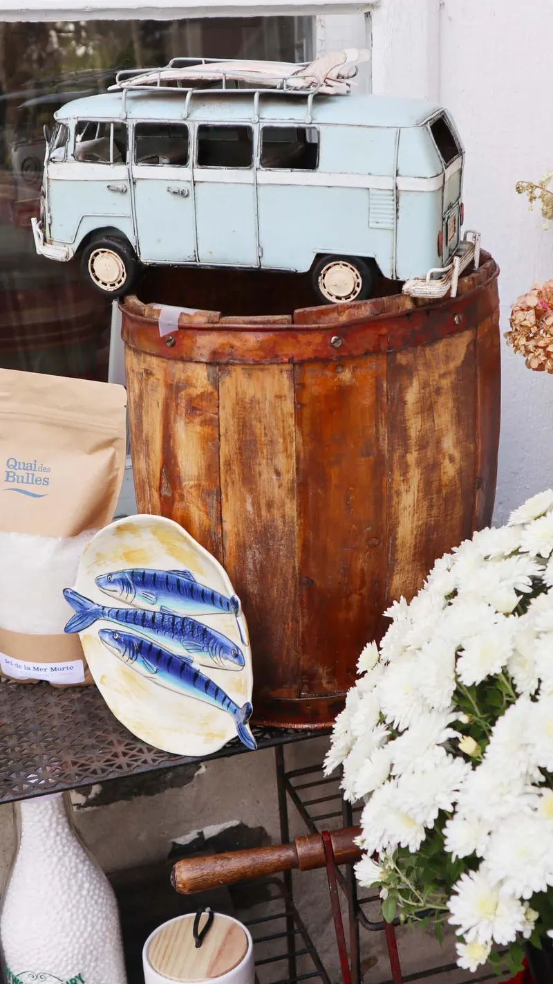Autobus Volkswagen miniature bleu pâle posé sur un baril en bois rouillé, assiette aux poissons bleus et chrysanthèmes blancs