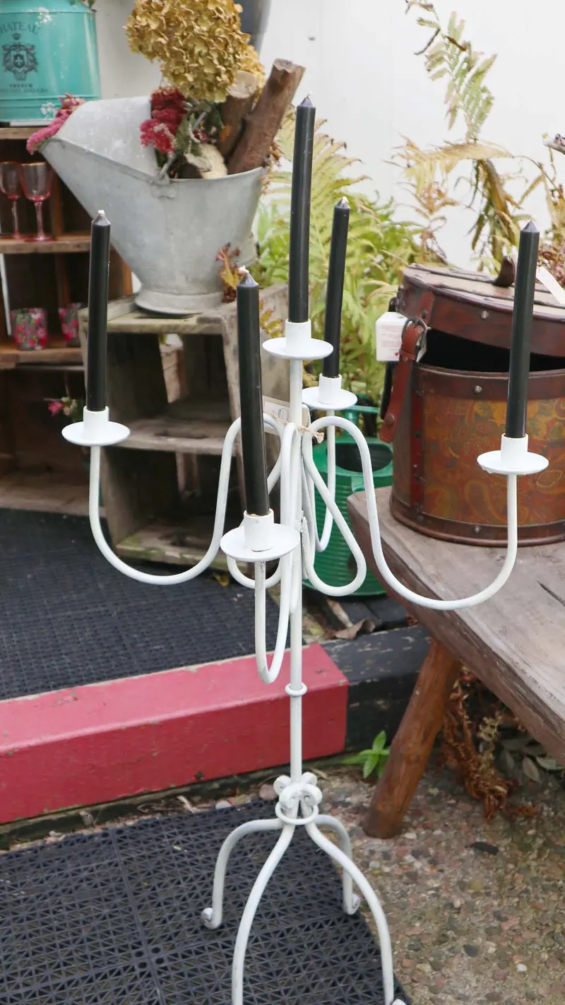 Candélabre blanc en fer forgé à cinq chandelles noires, devant un seau galvanisé garni de fleurs séchées